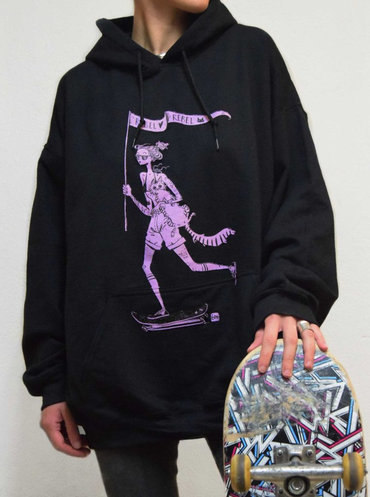 The girl is wearing a black hoodie with the rebel print. It is a design with a girl doing skate and holding a fluffy cat
